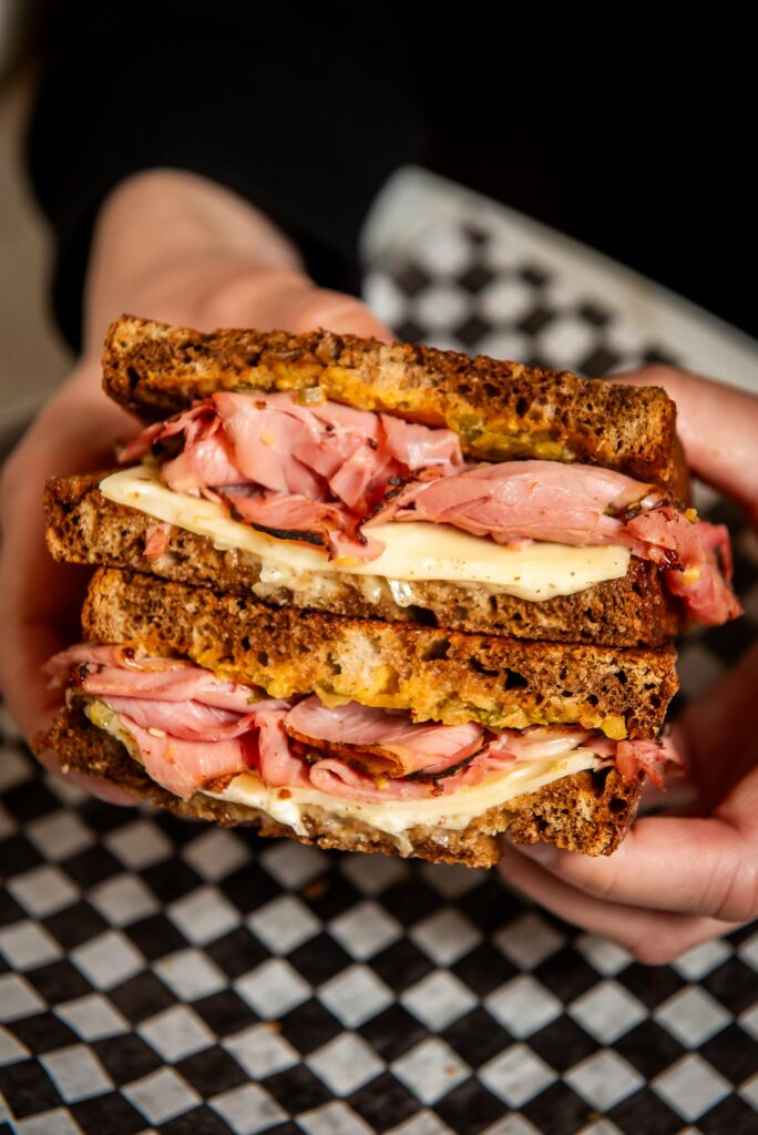 person holding a reuben sandwich against checkered paper